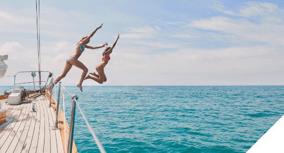 Viajes en familia. Experiencias para todos. Dos chicas saltan al agua desde la cubierta de un barco
