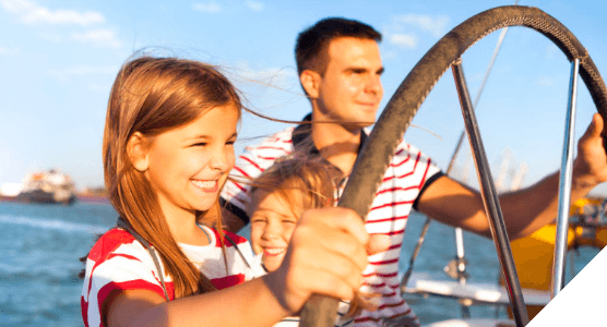 Viajes en familia. Experiencias para todos. Una niña sonriente maneja el timón de un barco con su padre y su hermana