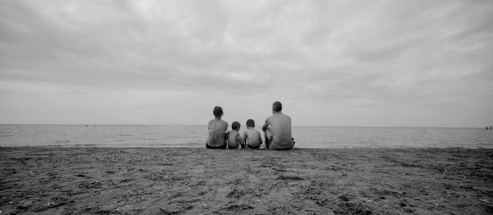 Viajes en familia. Una familia con niños sentados en la playa mirando al mar