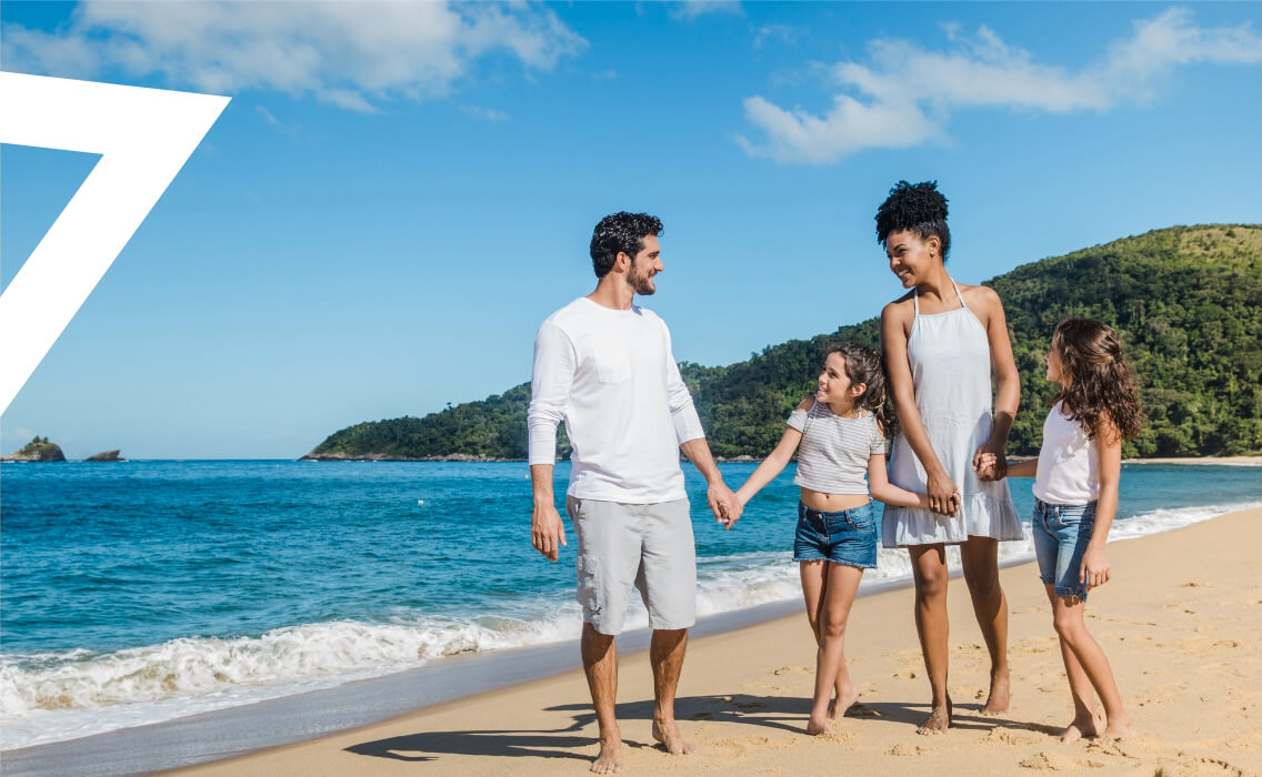 Viajes en familia. Una familia con niñas sonriente pasea por la playa