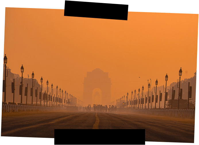 Viajes a medida. Viajes que inspiran. En un atardecer anaranjado se adivina entre niebla la Puerta de la India en Nueva Delhi