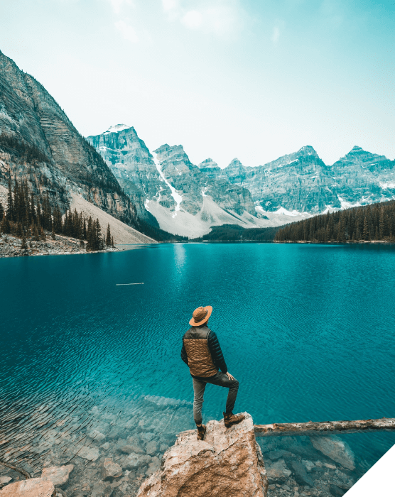 Viajes de novios. Verano. Un hombre subido en una roca frente a un lado mira las montañas nevadas en Canadá