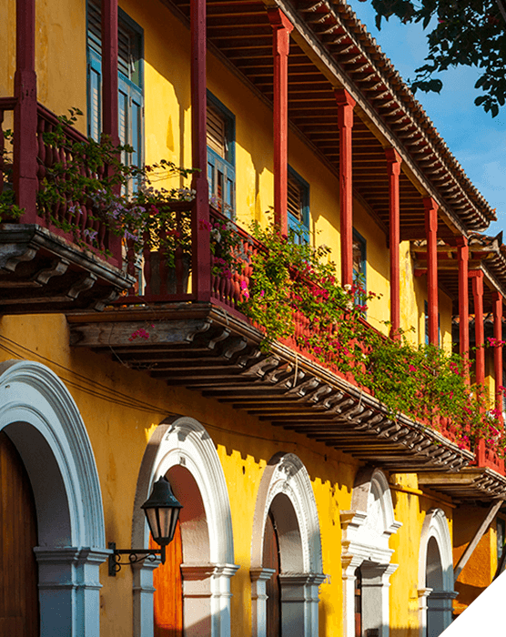 Viajes de novios. Invierno. Casa colonial de color ocre amarillo con arcos blancos, balconadas rojas y ventanas verdes en Cartagena de Indias, Colombia
