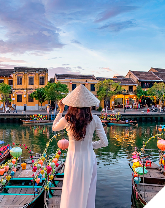 Viajes de novios. Invierno. Mujer vestida con ropa tradicional vietnamita en un canal con barcos decorados con farolillos de colores