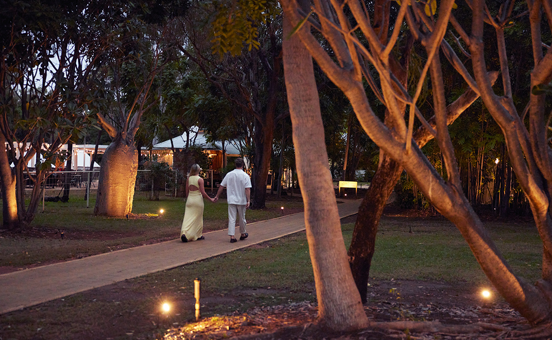Pareja paseando en un jardín de lujo al anochecer.