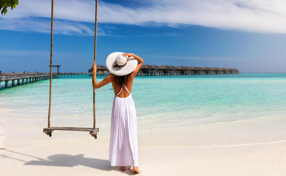 Mujer en un columpio frente a una playa paradisíaca y exclusiva.
