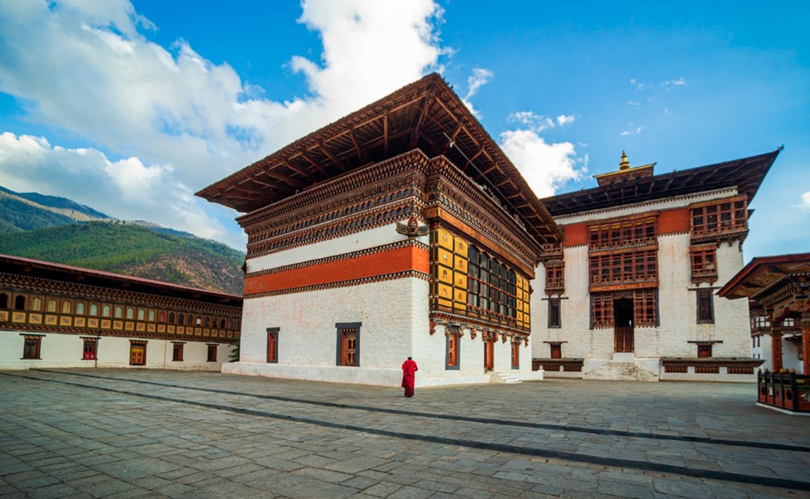 Monje budista caminando entre los muros de un monasterio en Bután, símbolo de la calma y conexión interior que definen los viajes de lujo y espiritualidad en el Himalaya.