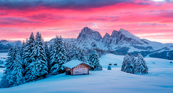 Amanecer invernal sobre una cabaña de montaña en los Dolomitas, símbolo de hospitalidad y elegancia alpina en un viaje de lujo a medida.