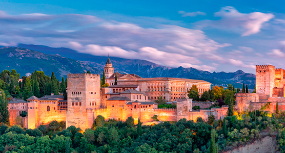 La Alhambra de Granada iluminada de noche con las montañas al fondo, ideal para un viaje de lujo a medida entre arte e historia