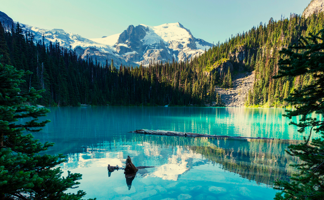 Lago de aguas cristalinas con montañas nevadas en la Columbia Británica, Canadá, escenario de un viaje de lujo a medida por paisajes naturales poco explorados