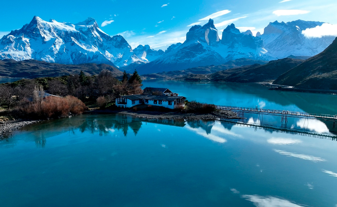 Vista de casas frente al lago y las cumbres de Torres del Paine al anochecer, en un paisaje único de la Patagonia chilena.