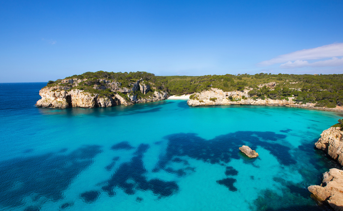Costa de Menorca en primavera, con pequeños acantilados, naturaleza mediterránea y aguas cristalinas.