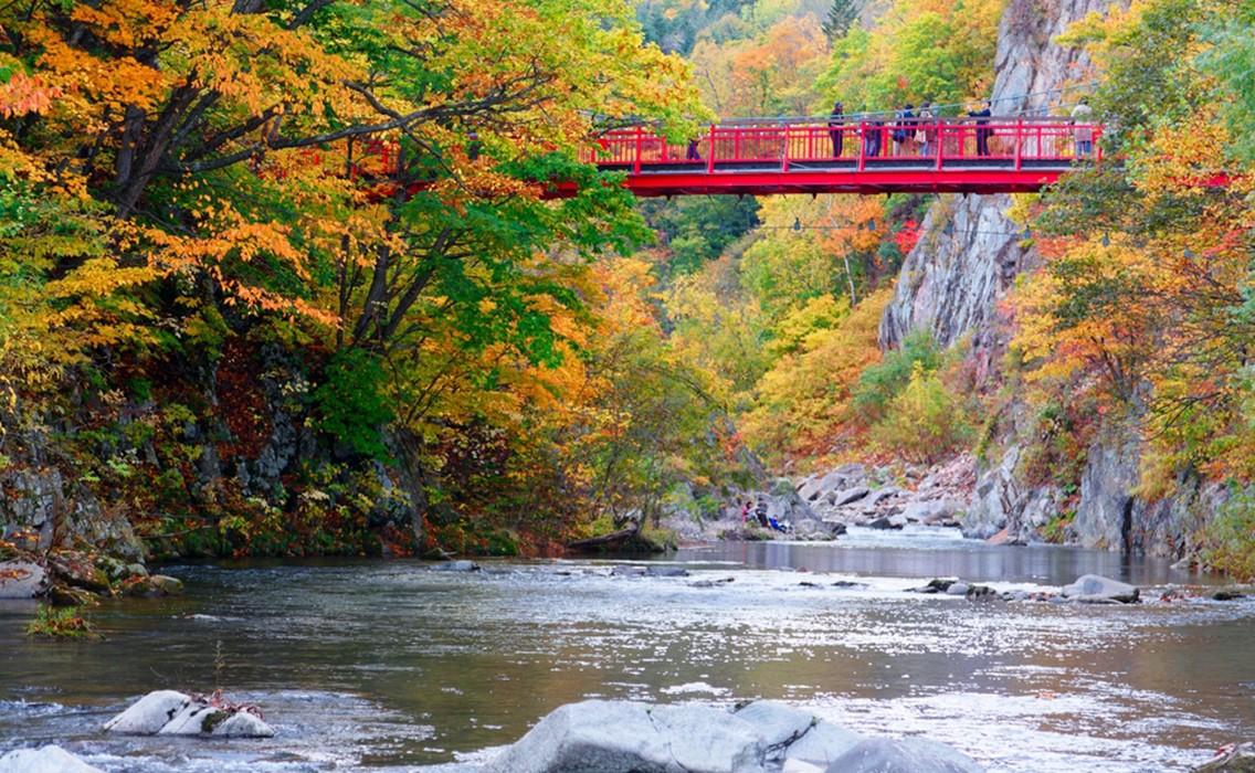 Puente colgante rojo de Futami sobre el río Toyohira en Jozankei, Sapporo, Hokkaido, rodeado de acantilados y naturaleza.
