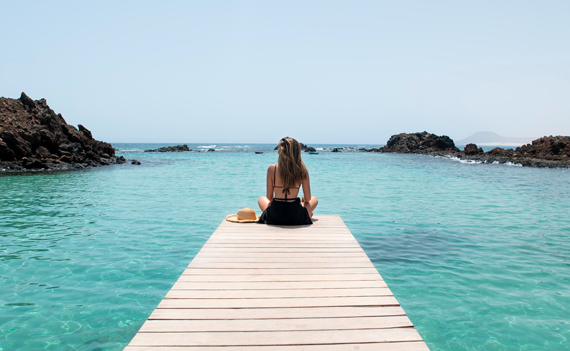 Viajera sola en una pasarela que se adentra en el mar al atardecer, disfrutando de un viaje a medida pensado para desconectar y recuperar el equilibrio.