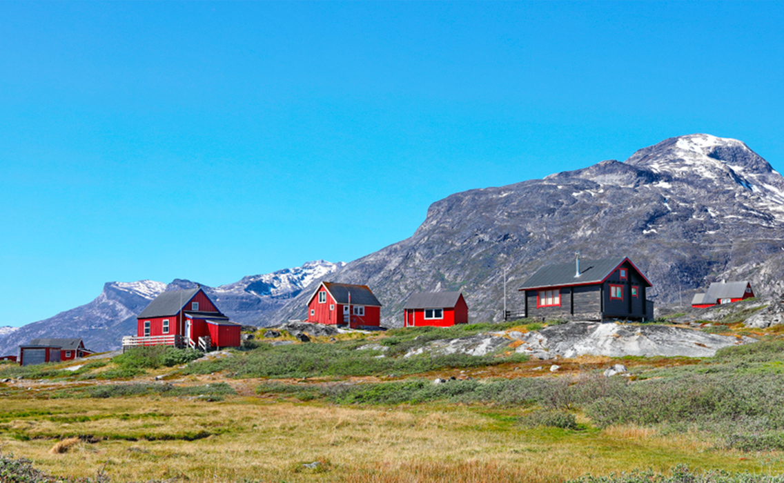 Pequeñas casas rojas junto a las montañas de Groenlandia, un paisaje ártico donde naturaleza y tradición conviven en armonía.