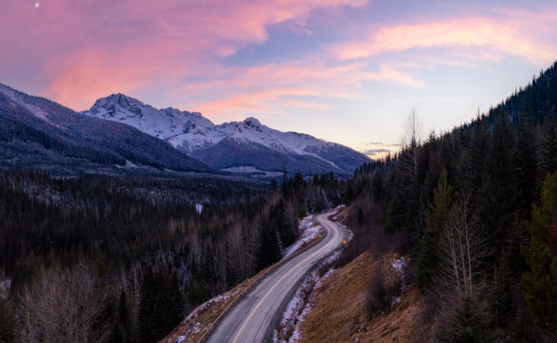 Bosque de pinos nevados y carretera panorámica al atardecer en la Columbia Británica, un paisaje icónico de la naturaleza canadiense.